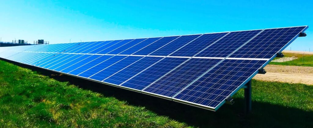 Imagem de um painel solar sob a grama e acima um céu azul para ilustrar usina de placas solares: o que é, como funcionam e por que são importantes para economia do país (e da sua)