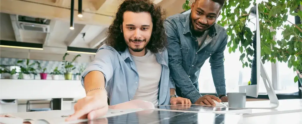 Dois homens inclinados sob uma mesa e uma placa solar avaliando como investir em energia solar