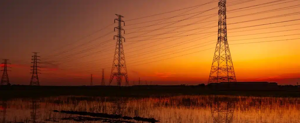 Quatro torres de linhas de transmissão de energia em ordem decrescente em frente a um pôr do Sol alaranjado para o artigo sobre projetos de energia limpa no Brasil