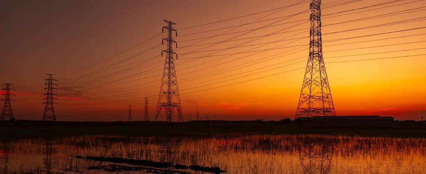 Quatro torres de linhas de transmissão de energia em ordem decrescente em frente a um pôr do Sol alaranjado para o artigo sobre projetos de energia limpa no Brasil