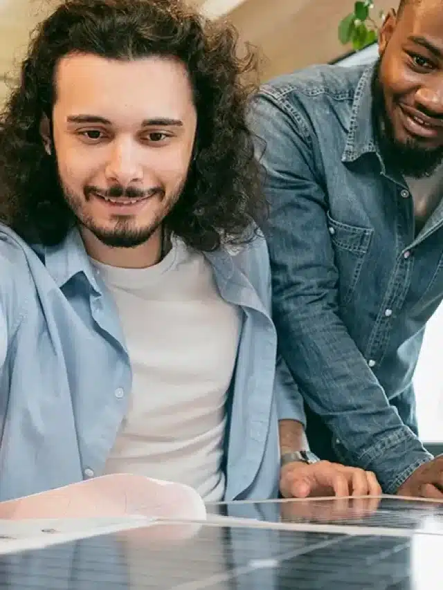 Dois homens inclinados sob uma mesa e uma placa solar avaliando como investir em energia solar