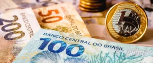 Na imagem aparecem três cédulas de reais nos valores de 50 reais, 200 reais e 100 reais, do lado direito inferior ao lado esquerdo superior, respectivamente. Ao lado da cédula de 100 reais aparece uma moeda de um real com as bordas douradas e o centro prata de frente. Imagem usada para exemplificar artigo sobre tempo de retorno do investimento em energia solar