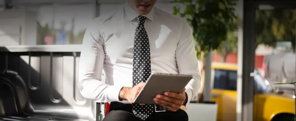 Um homem de camisa branca, gravata cinza semi sentado numa mensa segurando um ipad para exemplificar o artigo sobre "Empresa de energia solar: tudo que precisa saber antes de contratar uma"