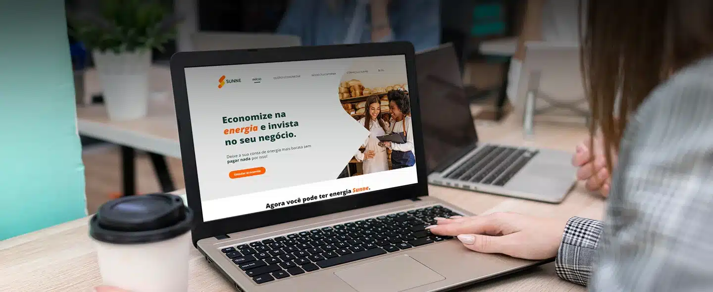 Na imagem tem um laptop com a página inicial do site da Sunne e na direita abaixo tem uma mulher jovem desfocada com a mão por cima do teclado do laptop para exemplificar artigo sobre "8 estratégias para conseguir energia solar barata para sua empresa".