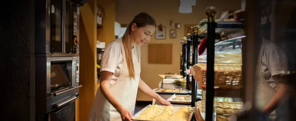 Mulher em padaria, próxima ao balcão segurando uma bandeja de croissants que vão ao forno, exemplificar artigo sobre Geração distribuída e o potencial da energia solar por assinatura