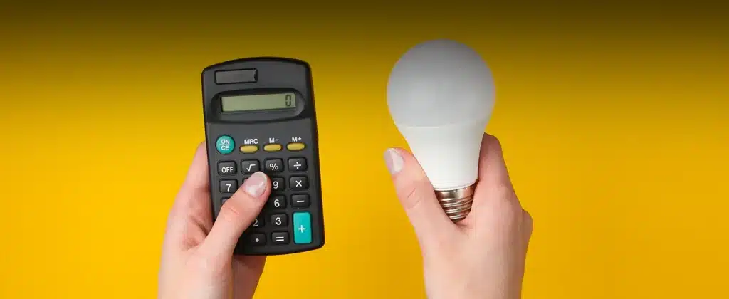 Fundo amarelo e duas mãos segurando uma calculadora e uma lampada LED para exemplificar artigo sobre Quem tem conta de energia solar paga menos?