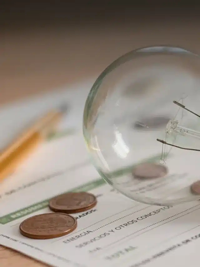 Imagem com uma lampada quebrada, algumas moedas na mesa, lápis e calculadora sobre um pedaço de papel para exemplificar artigo sobre Saiba se a conta de luz com energia solar fica mais barata