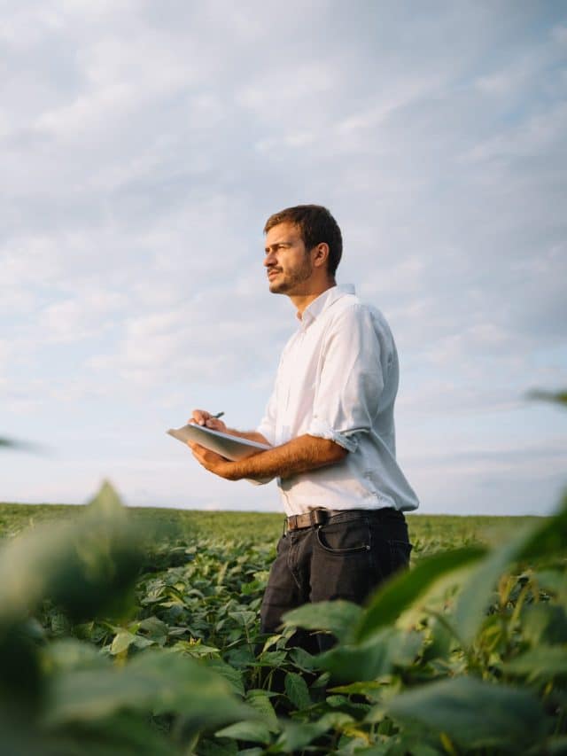 Young farmer in filed examining soybean corp. He is thumbs up.