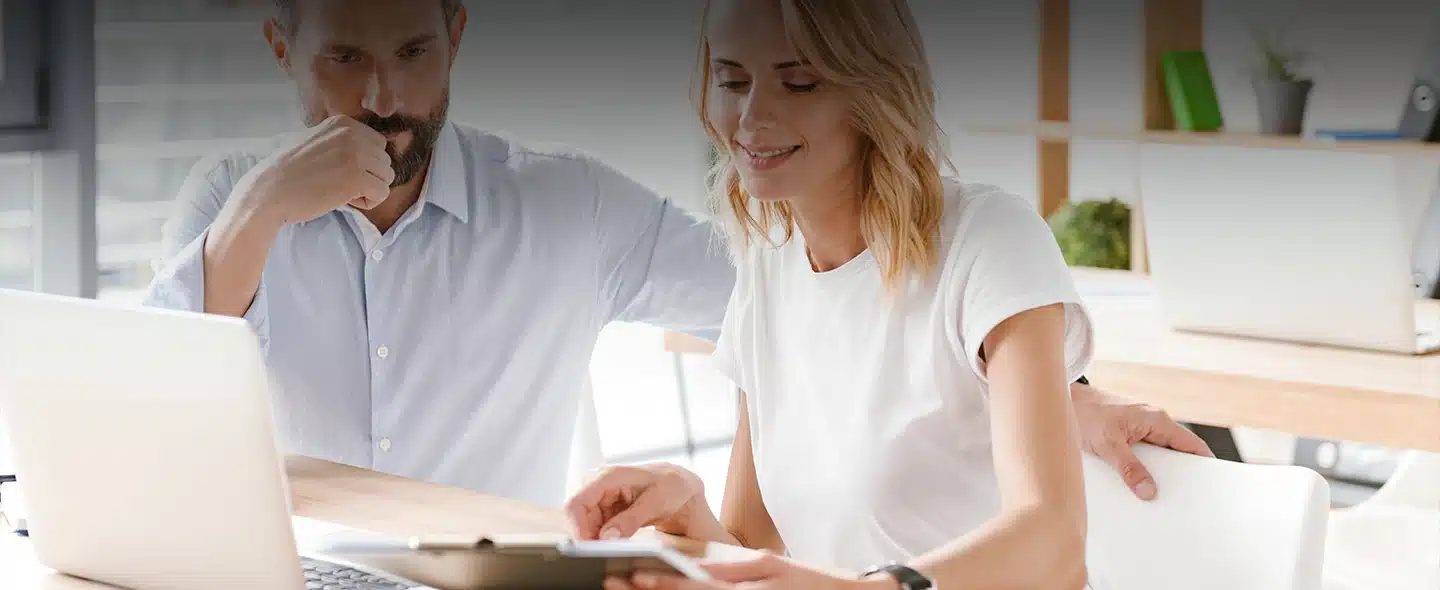 Homem e mulher com roupa branca em frente um laptop branco enquanto usam e olhem uma prancheta com atenção para artigo de 5 formas de economizar energia