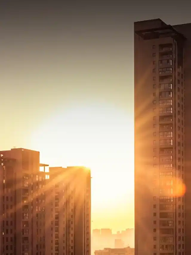 Imagem com coloração alaranjada de prédio e o céu com um sol brilhante ao fundo para artigo sobre Energia solar para condomínio: saiba como colocar no seu