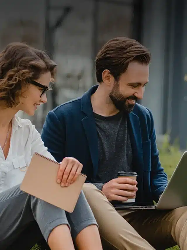 Homem e mulher sentados na grama olhando o laptop enquanto sorriem para artigo sobre As vantagens das tecnologias sustentáveis no Brasil