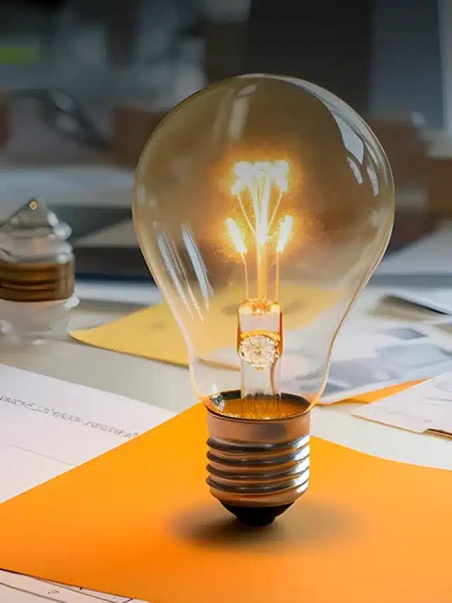 Mesa cheia de folhas brancas e marrons e objetos de escritório e uma lâmpada acessa na vertical em cima mesa para artigo sobre Entenda por que o ESS é cobrado no Mercado Livre de Energia