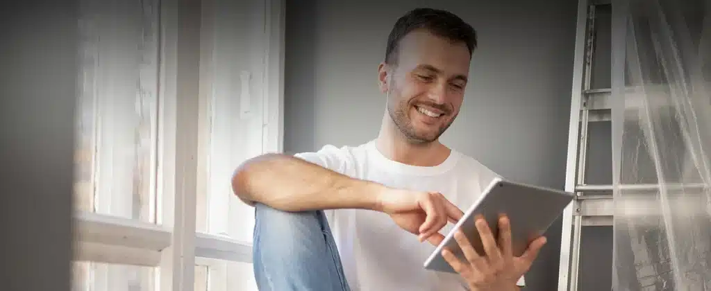 Homem jovem sorrindo e olhado um tablet para artigo Entenda como funciona energia por assinatura para empresas