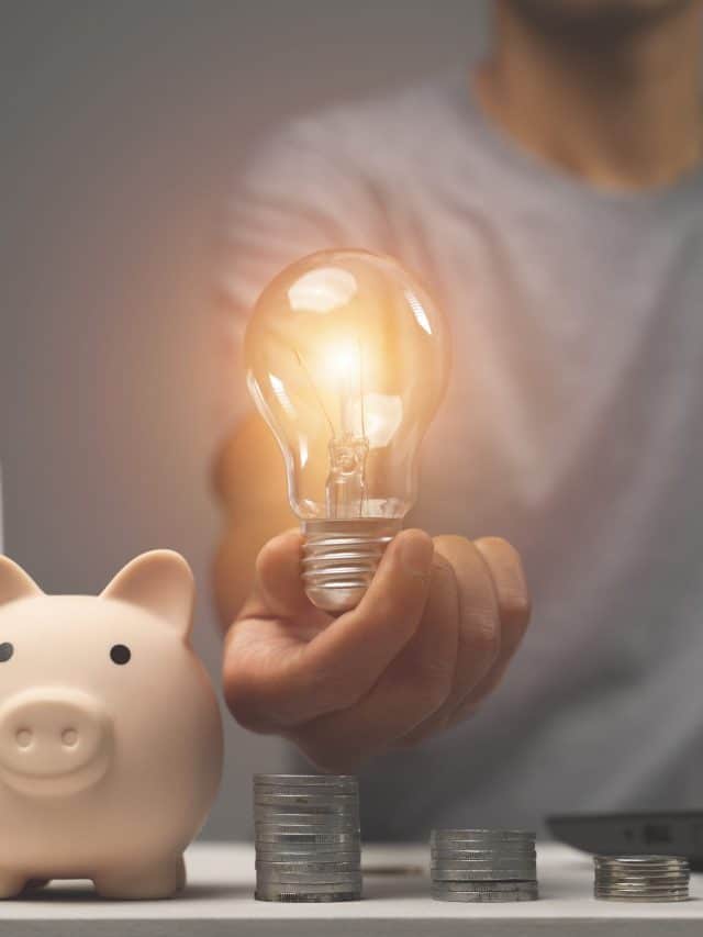 man holding lightbulb on piggy bank and coins stacking on desk.