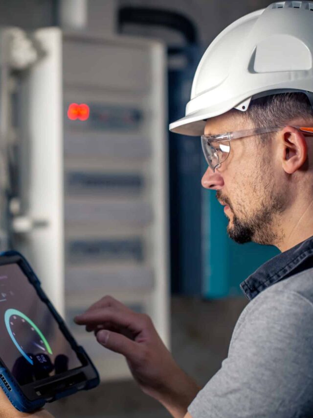 Man, an electrical technician working in a switchboard with fuses, uses a tablet.