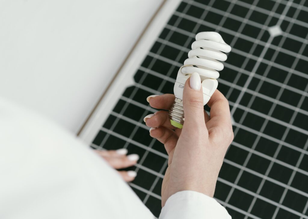 Mão segurando uma lâmpada ecológica sobre painel solar, simbolizando escolhas sustentáveis entre mercado livre x mercado cativo de energia.