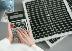 Pessoa calculando custos ao lado de painéis solares, simbolizando o investimento em uma micro usina solar e o retorno financeiro com energia limpa.