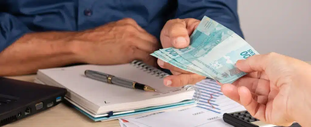 Homem de negócios dando cédulas de reais para parceiro durante contrato de energia por assinatura