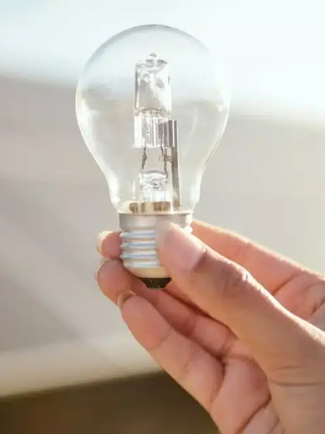 Mão segurando uma lâmpada em frente a painéis solares