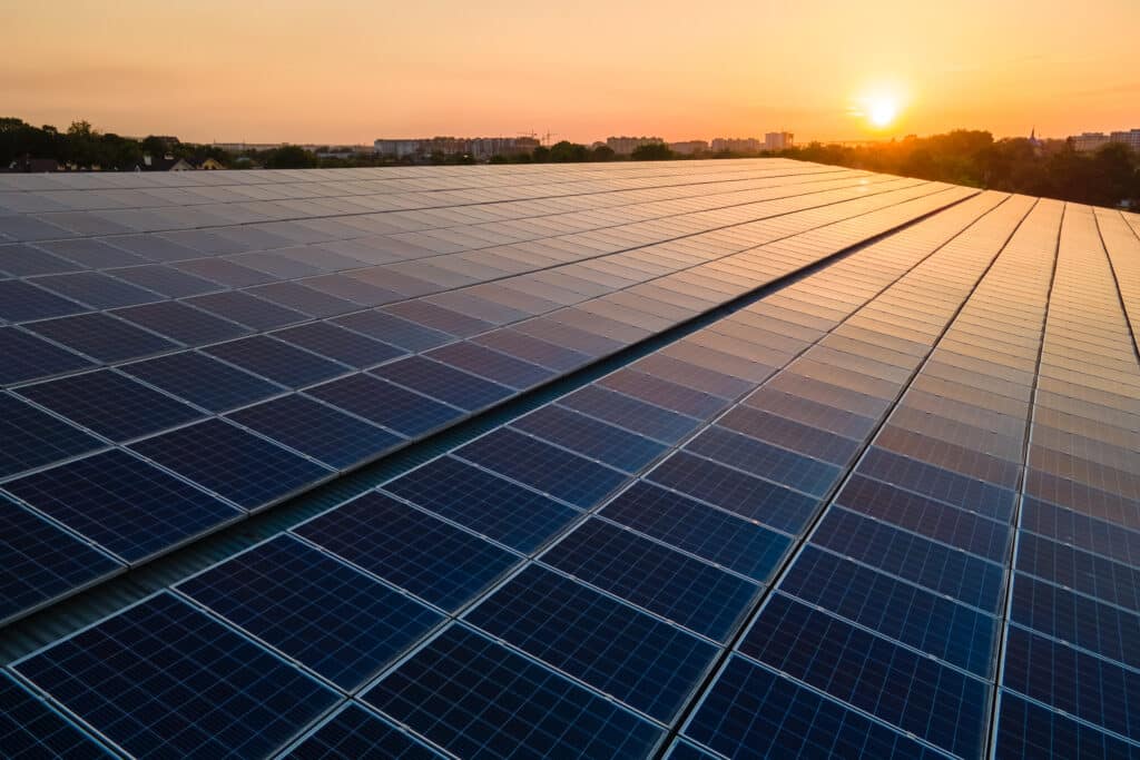 Vista aérea de uma usina solar com centenas de painéis fotovoltaicos alinhados, captando energia ao pôr do sol, simbolizando a produção em larga escala e o uso de plataforma de gestão para usinas solares.