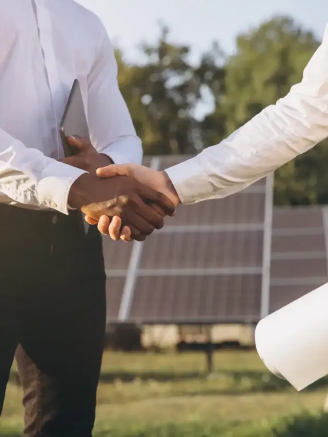 Empresários selando parceria com aperto de mãos em frente a usinas solares, representando o desafio da captação de clientes para usinas solares e como superá-lo.