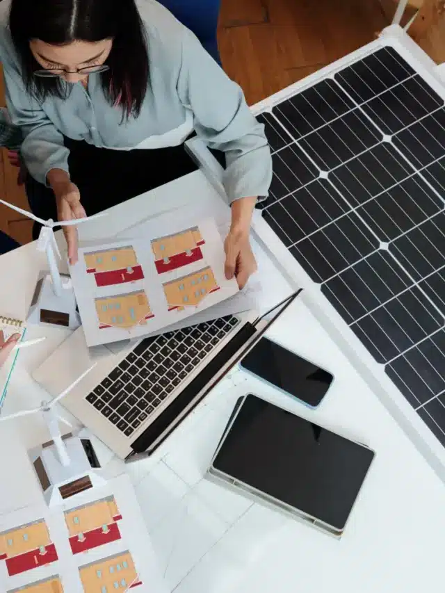 Dois profissionais analisando projetos arquitetônicos e modelos de energia solar ao lado de um painel fotovoltaico, com apoio de um software de gestão para usinas solares.