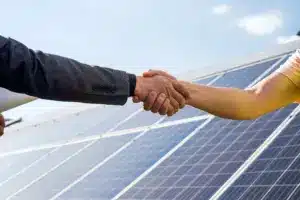 Duas pessoas apertando as mãos em frente a painéis solares, simbolizando parceria e contrato de locação de energia solar para projetos sustentáveis.
