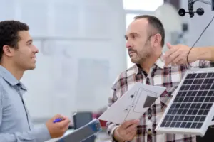 Dois profissionais discutindo relatórios técnicos ao lado de um painel solar, ilustrando a importância do pós-venda em energia solar.