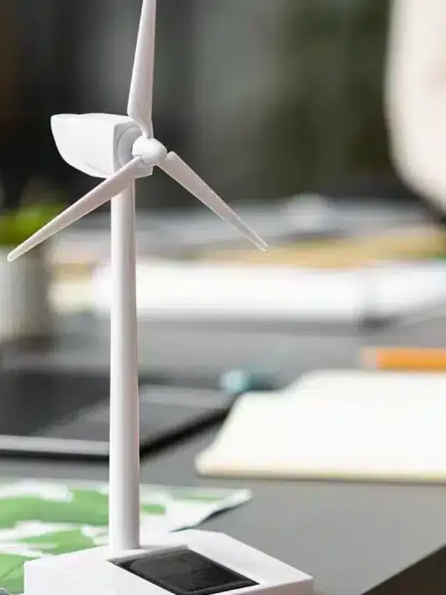 Ambiente de trabalho com laptops e miniaturas de turbinas eólicas sobre a mesa, simbolizando planejamento e gestão de créditos para usinas de energia renovável.