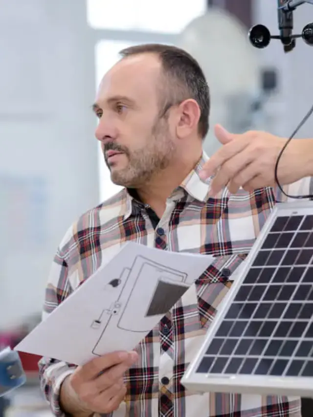 Dois profissionais discutindo relatórios técnicos ao lado de um painel solar, ilustrando a importância do pós-venda em energia solar.