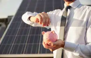 Gestão de inadimplência em energia solar representada por uma usina solar ao fundo e a mão de um investidor colocando dinheiro em um cofrinho de porquinho, simbolizando segurança financeira e retorno de investimento.