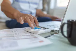 Pessoa usando calculadora para conferir duas faturas de energia por assinatura.