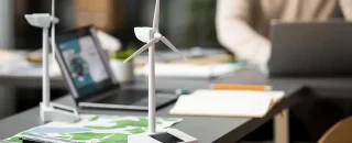 Ambiente de trabalho com laptops e miniaturas de turbinas eólicas sobre a mesa, simbolizando planejamento e gestão de créditos para usinas de energia renovável.