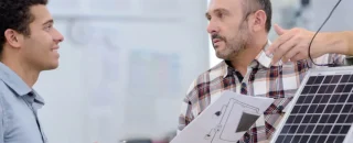 Dois profissionais discutindo relatórios técnicos ao lado de um painel solar, ilustrando a importância do pós-venda em energia solar.