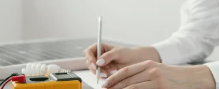 Pessoa escrevendo em papel ao lado de um painel solar e equipamentos de medição, simbolizando planejamento e gestão em energia por assinatura.