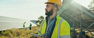Engenheiro em campo com tablet supervisionando painéis solares, representando a gestão de usinas solares.