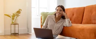 Jovem moça alegre trabalhando em seu laptop agora que economiza com energia solar por assinatura