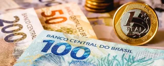 Na imagem aparecem três cédulas de reais nos valores de 50 reais, 200 reais e 100 reais, do lado direito inferior ao lado esquerdo superior, respectivamente. Ao lado da cédula de 100 reais aparece uma moeda de um real com as bordas douradas e o centro prata de frente. Imagem usada para exemplificar artigo sobre tempo de retorno do investimento em energia solar