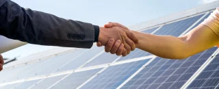 Duas pessoas apertando as mãos em frente a painéis solares, simbolizando parceria e contrato de locação de energia solar para projetos sustentáveis.
