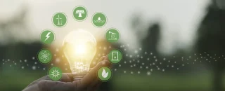 Mão segurando uma lâmpada iluminada com ícones de fontes limpas ao redor, representando o uso de energia renovável no setor alimentício para promover sustentabilidade, economia e inovação na produção de alimentos.