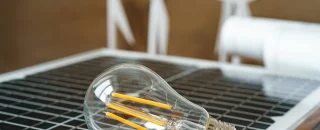 Painel solar com lâmpada de LED e turbinas eólicas ao fundo, representando fontes renováveis e as vantagens do mercado livre de energia para empresas que buscam economia e sustentabilidade.