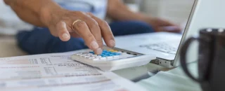 Pessoa usando calculadora para conferir duas faturas de energia por assinatura.